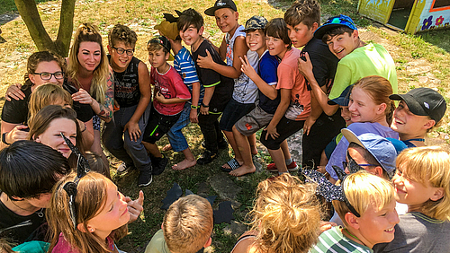 Gemeinsam mehr erleben: Das Kinder- und Jugend-Outdoor-Camp der Hochschule Mittweida verbindet Erlebnispädagogik und Technik. (Foto: Markus Lohse) Das Bild zeigt von schräg oben eine Polonaise im Kreis mit 20 fröhlich lachenden Kindern und zwei jungen Frauen.