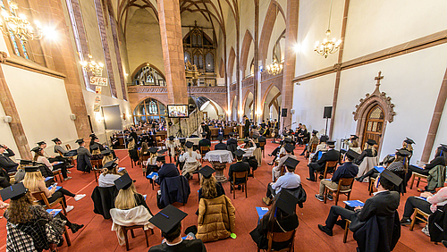 Behüteter Blick der Absolvent:innen ins Kirchenschiff auf Professor:innen und Angehörige, die durch das Studium begleitet haben.