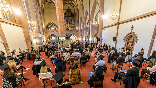 Behüteter Blick der Absolvent:innen ins Kirchenschiff auf Professor:innen und Angehörige, die durch das Studium begleitet haben.