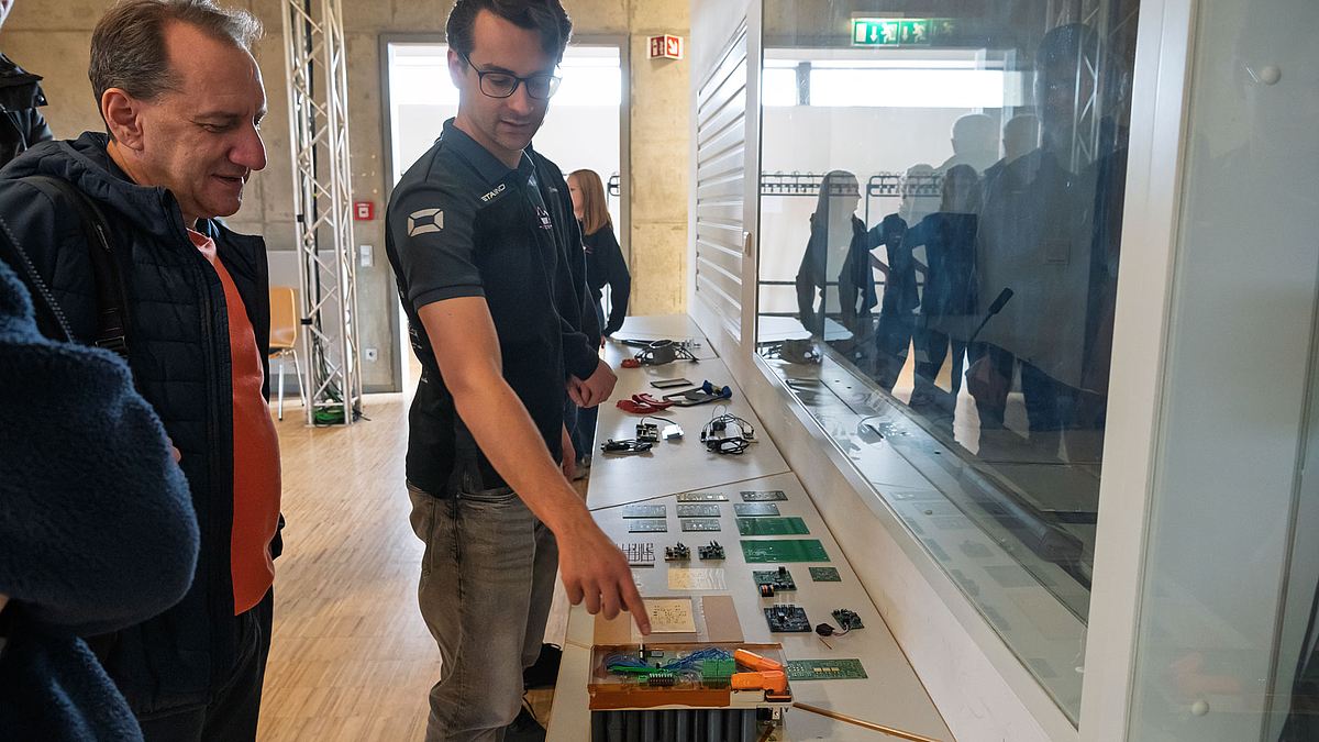 Zwei männliche schauen auf Bauteile, die auf Tischen ausgelegt sind.