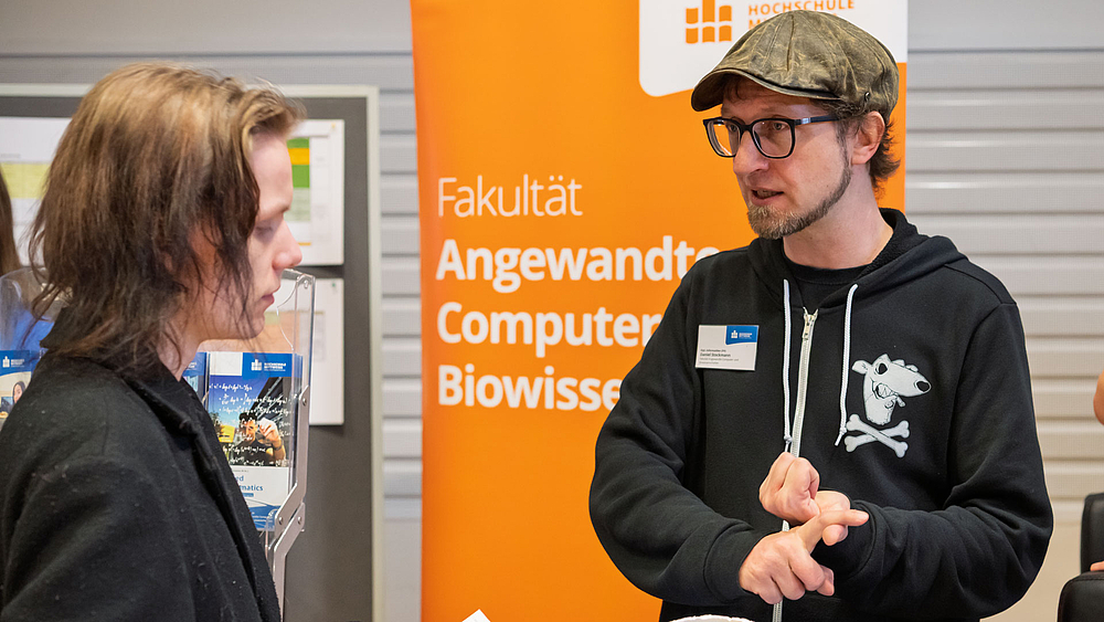 Zwei männliche Personen im gespräch vor Rollup "Fakultät Angewandte Computer und Biowissenschaften".