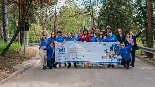 Die Hochschulallianz EURECA-PRO vernetzt neben Lehrenden und Forschenden auch die Studierenden von neun Hochschulen in der Europäischen Union. (Foto: Alex Bogye/EURECA-PRO) 15 Studierende halten auf einem Gruppenbild einen großen Mesh-Banner mit einem Aufdruck der Hochschulallianz EURECA-PRO in die Kamera.