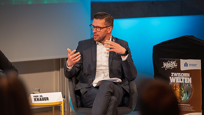Professor Alexander Knauer sitzt auf einem Panel und gestikuliert entspannt.